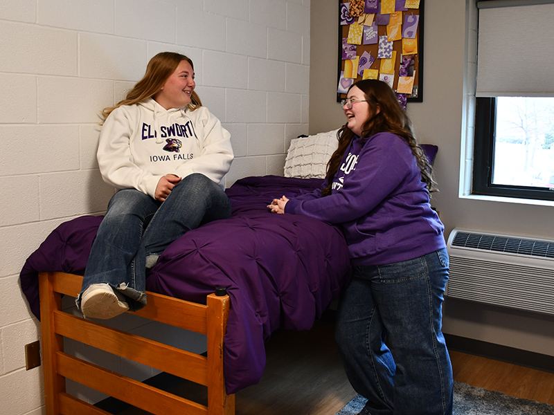 Students hanging out in their dorm room, sitting on the bed. 