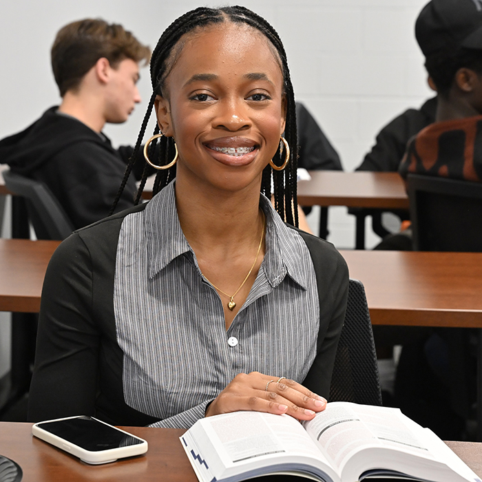 student smiling at camera with bible on table in front of her