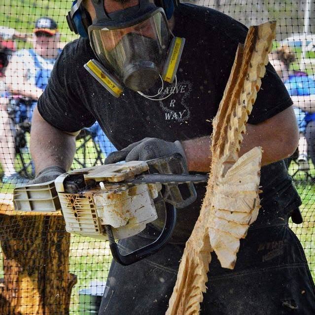 man wearing a respirator mask carving an eagle out of a log using a chainsaw